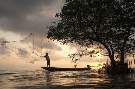 Silhouette of Fishermen throwing net fish on sunset time in a lake.の写真素材