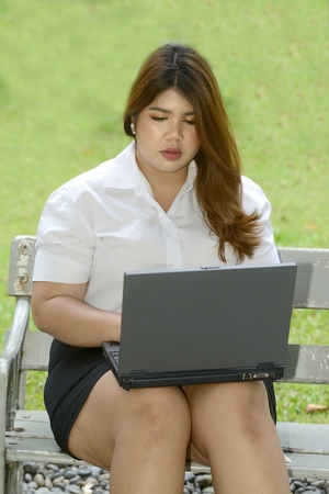 Pretty Asian fat woman pose working with laptop on a chair in the park.の写真素材