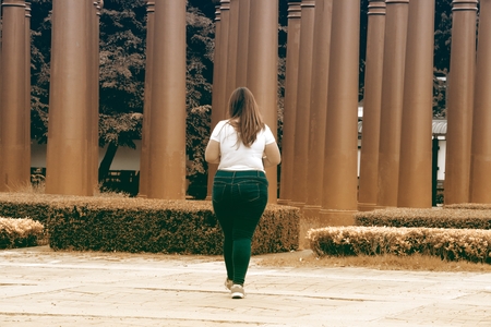 Asian pretty smiley face fat woman pose walking and hold a booklet on group of pole in the park.の写真素材