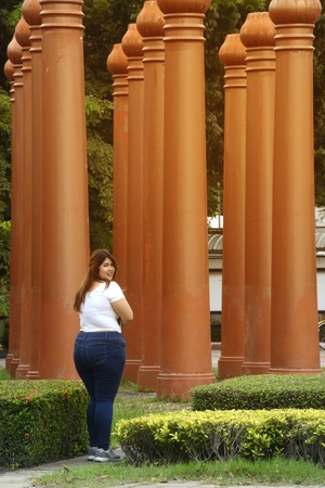 Asian pretty smiley face fat woman pose walking and hold a booklet on group of pole in the park.の写真素材