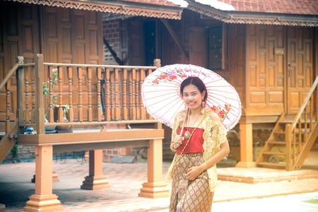 Portrait of Asian female in traditional dresses pose a holding umbrella at Thai home.の写真素材