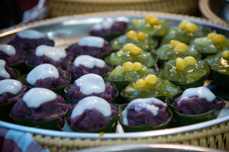 Thai dessert sweet is Creamy Coconut Tapioca and Corn Pudding with Coconut Ta-go topping and wrapped with banana leaves on wooden background.の写真素材