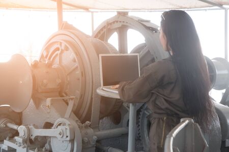 Pretty Asian female soldier working with laptop on a ship.