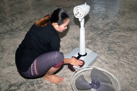 The housekeeper is assembling and installing an electric fan after cleaning.
