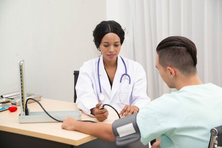 African female doctors measure blood pressure of male Caucasian patients with a blood pressure...