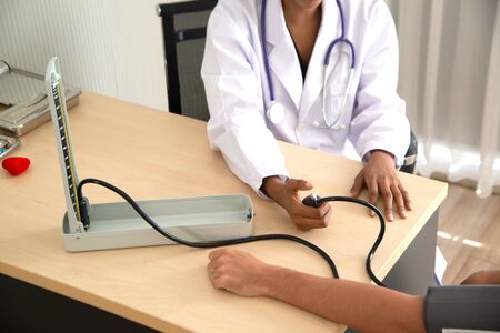 African female doctors measure blood pressure of male Caucasian patients with a blood pressure...