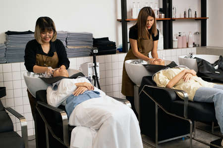 A hairdresser washes hair for a customer in a barber shop and women lying on a chair in a robe which takes care of the hair and scalp professionally.の写真素材