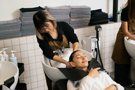 A hairdresser washes hair for a customer in a barber shop and women lying on a chair in a robe which takes care of the hair and scalp professionally.の写真素材