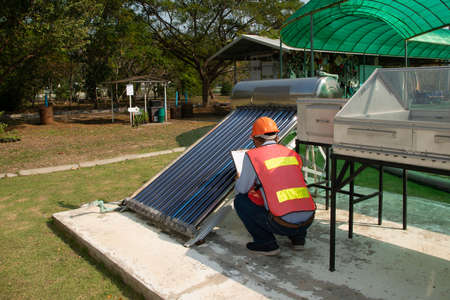 The Asian worker in uniform and helmet checks concentrating Solar Power with Flat Plat collector and...