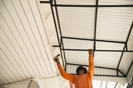 Male worker paints the awning of the house black with paint brush.