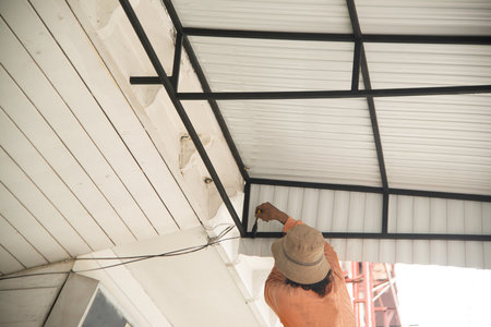 Male worker paints the awning of the house black with paint brush.