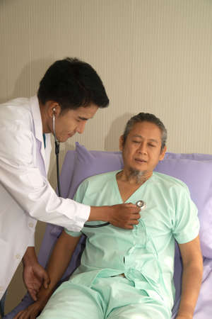 An Asian male doctor examining an elderly Asian male patient using a cardiac stethoscope in a...