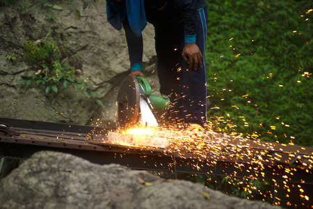 A professional craftsman is cutting metal with a rotatable diamond blade. To make an outdoor bridge...