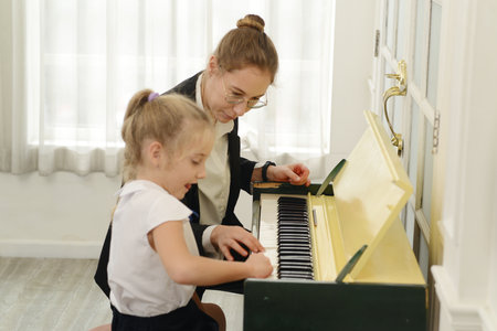 A young white teacher is teaching and training a little girl to play the piano. which is a classic education for kids, learning art.の写真素材