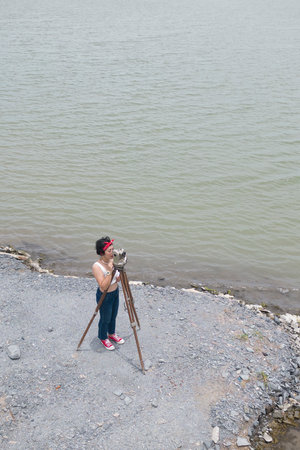 Pretty Asian female surveyor or engineer worker working with theodolite transit equipment at outdoor...