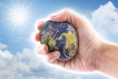 hand is holding to the stone world on blue sky backgroundの写真素材