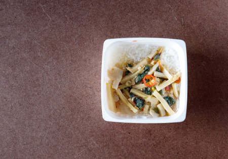 Stir-fried chicken with chili paste and bamboo shoots in food container on wood background.Top viewの写真素材