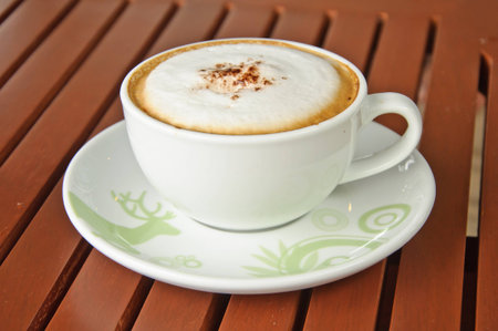 A cup of Capuchino coffee in a white cup on wooden background の写真素材