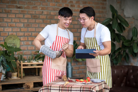 Young asian men couple friend using tablet while cooking in the kitchen at home for holiday festival celebration.. LGBT, Gay and love relationship conceptの写真素材