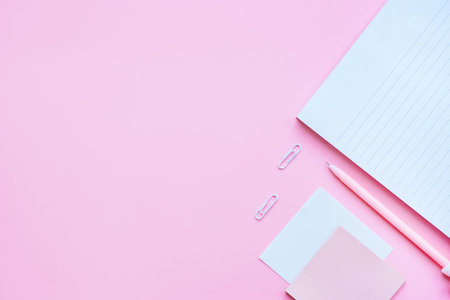 Beautiful office stationery flatlay with ruled notebook, pink pen, sticky note and paper clip on the bright desk with pink background.の写真素材