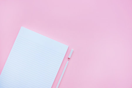Beautiful office stationery flatlay with ruled notebook and white pen on the bright desk with pink background.の写真素材