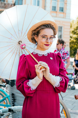 Kiev, Ukraine - May 12, 2018: Girl in vine red vintage dress and glasses with japanese umbrella participating in bicycle tweed run Retro cruise on May 12, 2018 in Kiev, Ukraine.のeditorial素材