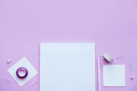 Beautiful office stationery flatlay with ruled notebook, pen, sticky note and paper clip on the bright desk with violet background.の写真素材