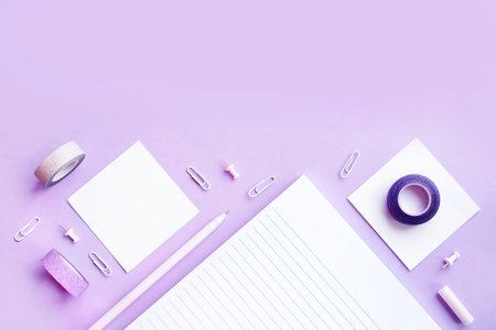 Beautiful office stationery flatlay with ruled notebook, pen, sticky note and paper clip on the bright desk with violet background.の写真素材