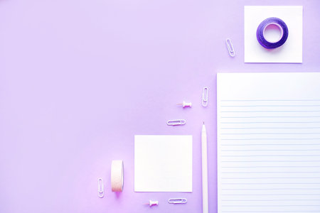 Beautiful office stationery flatlay with ruled notebook, pen, sticky note and paper clip on the bright desk with violet background.の写真素材