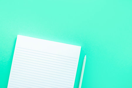 Beautiful office stationery flatlay with ruled notebook and white pen on the bright desk with turquoise background.の写真素材