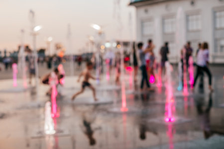 Blurred background with group of kids playing in the fountain on the hot summer evening.の写真素材