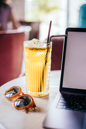 Beautiful glass of yellow passionfruit lemonade, trendy sunglasses and laptop on the wooden table....