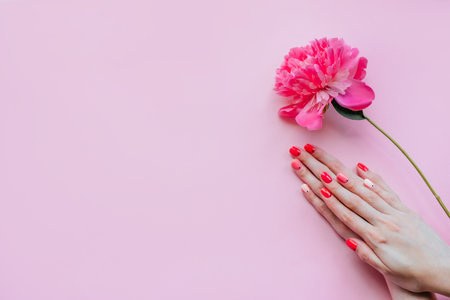 Creative bright trendy summer manicure with nails of different color. Female hands with art nail design on pink background and fuchsia peony flower.の写真素材