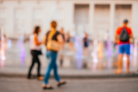 Blurred background with people watching the fountain on the hot summer evening.