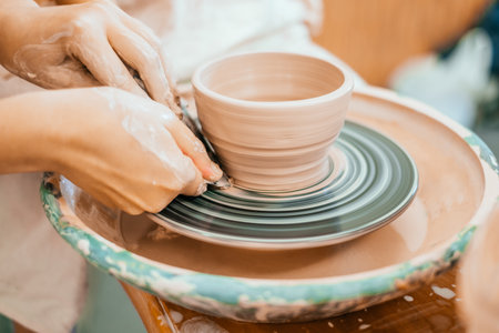 Women working on the potters wheel. Hands sculpts a cup from clay pot. Workshop on modeling on the potters wheel.の写真素材