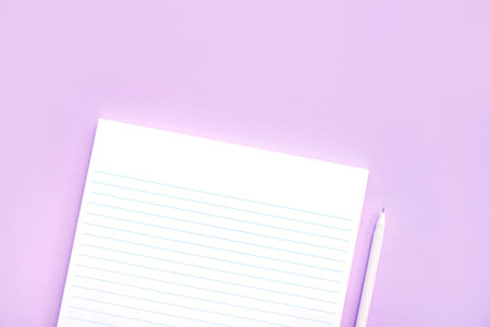 Beautiful office stationery flatlay with ruled notebook, pen, sticky note and paper clip on the bright desk with violet background.の写真素材