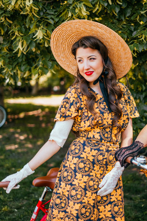 Kiev, Ukraine - May 12, 2018: Girl in floral print dress, straw hat, gloves and red lipstick participating in bicycle tweed run Retro cruise on May 12, 2018 in Kiev, Ukraine.のeditorial素材