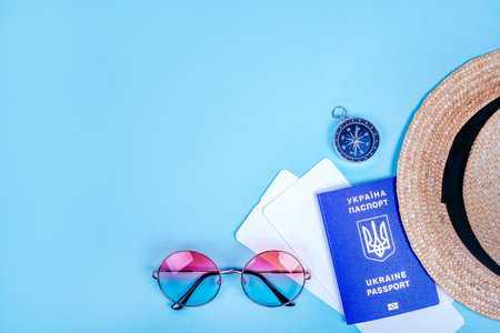 Travel flatlay with biometric passport, gradient round sunglasses, straw boater hat, compass and plane tickets on the bright blue background.の写真素材