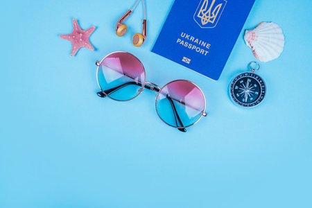 Travel flatlay with biometric passport, gradient round sunglasses, compass and rose gold earphones...