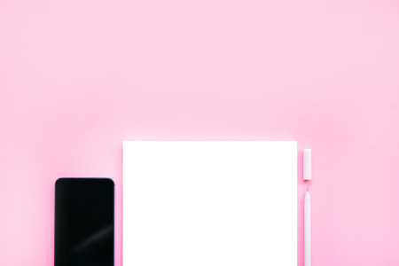 Beautiful office stationery flatlay with ruled notebook, white pen and smartphone on the bright desk with pink background.の写真素材