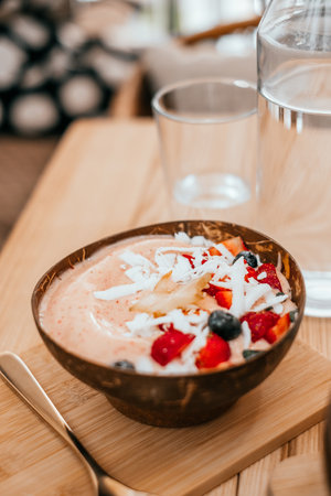 Beautiful pink strawberry smoothie bowl with coconut shavings, banana, blueberries and star fruit on the wooden table with gold spoon.の写真素材