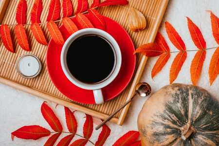 Autumn flatlay with cup of coffee with red plate on the wooden tray, gold spoon, candle, pumkin and red leaves.の写真素材