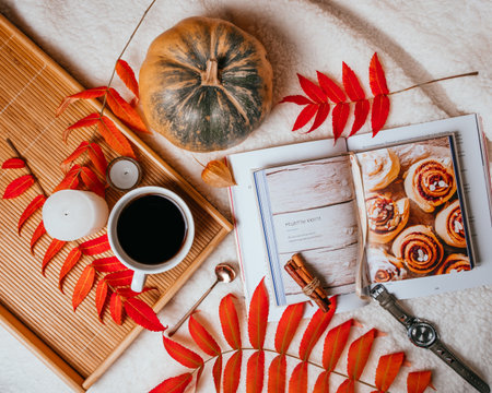 Autumn flatlay with cup of coffee, red plate on the wooden tray, gold spoon, candle, pumkin, cook book and red leaves.のeditorial素材