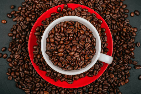 White cup of coffee on the red plate with roasted coffee beans on the black concrete stone background. Flatlay style.の写真素材