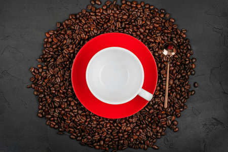 Empty white cup on the red plate with roasted coffee beans and gold spoon on the black concrete stone background. Flatlay style.の写真素材