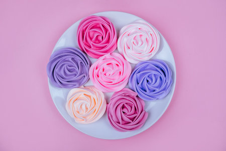Beautiful pink, magenta, orange and violet rose flower shaped meringue flatlay on the white round...