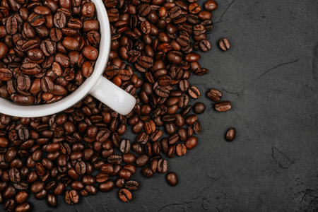 White cup full of with roasted brown coffee beans on the black concrete stone background. Flatlay style.の写真素材