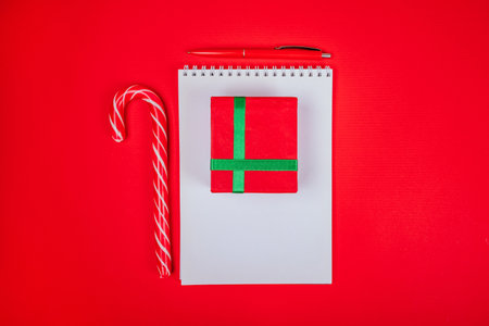 Christmas flatlay with red gift box, clean spring pad and candy canes on the bright red background.の写真素材