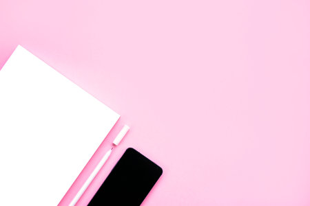 Beautiful office stationery flatlay with ruled notebook, white pen and smartphone on the bright desk with pink background.の写真素材
