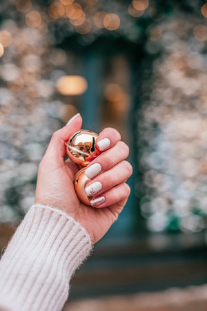 Closeup photo of a beautiful female hand with nude Christmas inspired manicure holding gold bells.